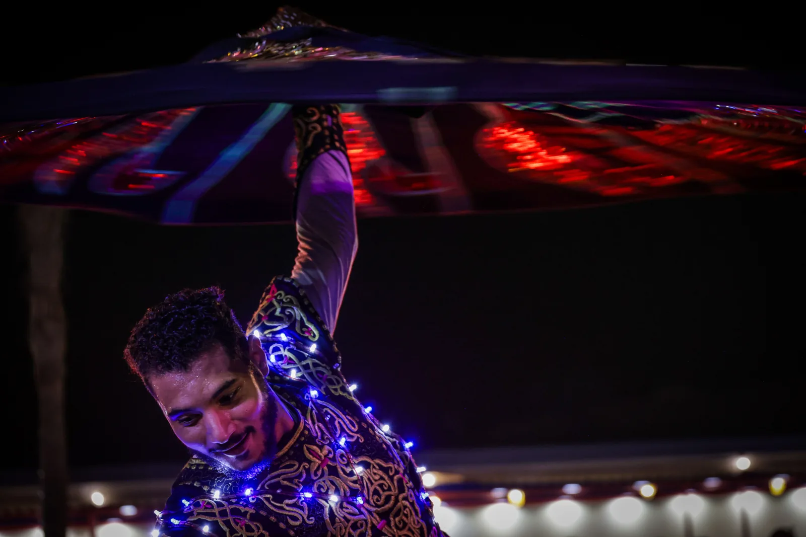 Gros plan sur un danseur de Tanoura tournoyant sous les projecteurs colorés de la scène, à la nuit tombée (photographie représentative, il ne s'agit pas de la scène d'Al Hadheerah)