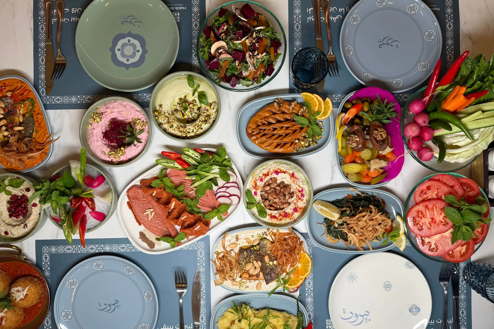 Vue plongeante sur un assortiment de mezze du Moyen-Orient avec dips, salades et plats grillés (photographie représentative du style de cuisine, il ne s'agit pas du buffet d'Al Hadheerah)
