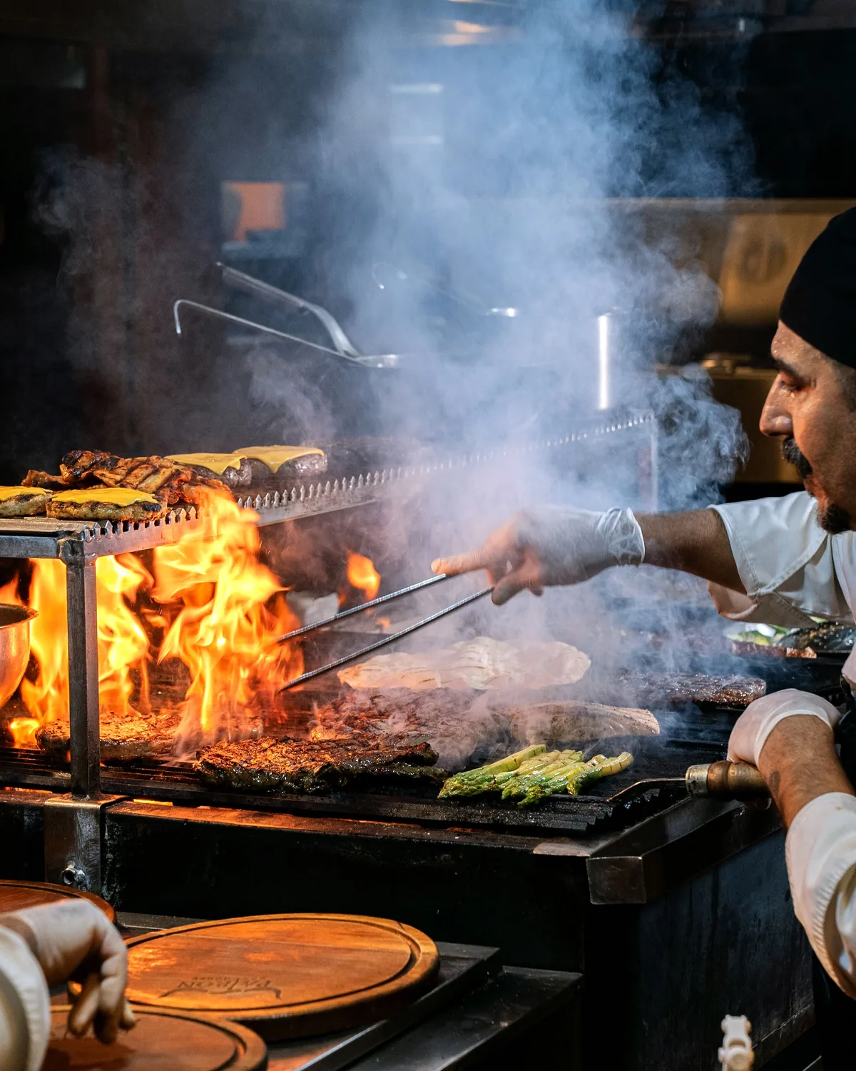 Un chef grillant viandes et légumes à la flamme vive sur un poste de cuisson en direct (photographie représentative de la cuisson au feu de bois)